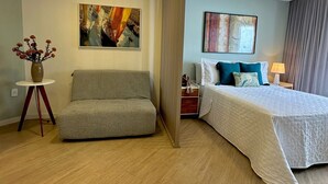 Et hotelværelse med en seng, en sofa, et lille bord med en vase og to billeder på væggen.