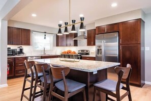 A modern kitchen with dark wood cabinets, a large island with bar stools, a stainless steel refrigerator, and a pendant light fixture. - Spacious Louisville home with backyard and parking (Louisville)