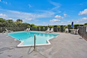 A rectangular swimming pool with a metal ladder, surrounded by white lounge chairs and a table with chairs, under a clear sky. - Oceanfront Corner Unit with Pool on Boardwalk (Carolina Beach)