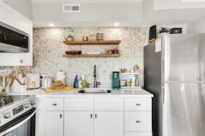 A modern kitchen with white cabinetry, stainless steel appliances, and decorative wall tiles. - Oceanfront Corner Unit with Pool on Boardwalk (Carolina Beach)