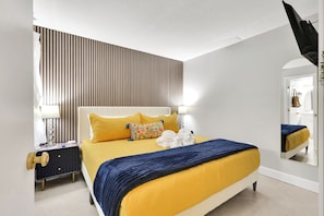 A bedroom with a bed, bedside tables, a mirror, and a striped wall. - Oceanfront Corner Unit with Pool on Boardwalk (Carolina Beach)