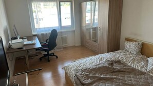 Ein Schlafzimmer mit Bett, Schreibtisch, Computer, Stuhl und Kleiderschrank.