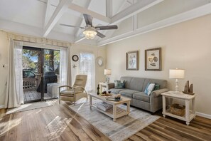 A living room with a ceiling fan, a sofa, a coffee table, a side table with a lamp, and a window with curtains. - Nautical Queen's Grant Villa, Single Level, Partial Lagoon View Patio & Grill (Hilton Head Island)