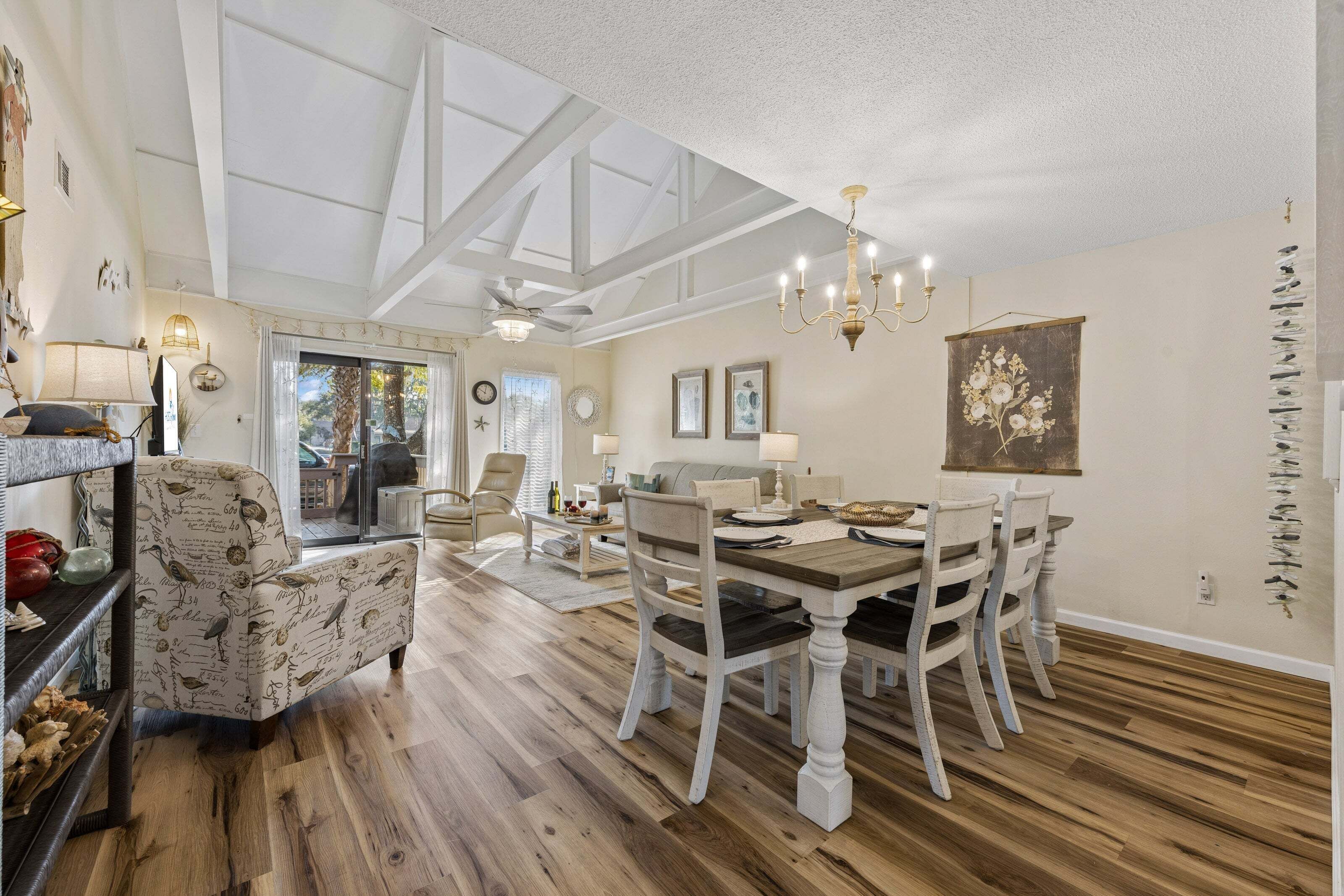 A dining area with a wooden table and chairs, a chandelier, and a view through a glass door to the outside.