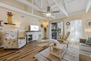 A living room with a ceiling fan, a television, a wooden coffee table, and a sofa. - Nautical Queen's Grant Villa, Single Level, Partial Lagoon View Patio & Grill (Hilton Head Island)