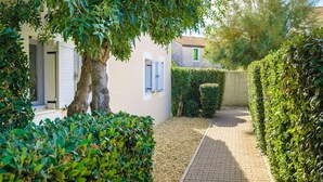 A narrow paved pathway flanked by neatly trimmed hedges and a building with a white facade and shuttered windows. - Residence Les Soleillades Et Scarlett (Palavas-les-Flots)