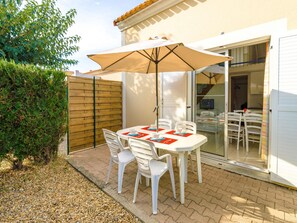 An outdoor patio with a table and chairs, a wooden fence, and a sliding glass door leading to an interior space. - Residence Les Soleillades Et Scarlett (Palavas-les-Flots)