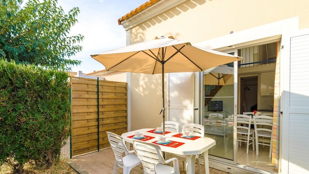 An outdoor patio with a table and chairs, a wooden fence, and a sliding glass door leading to an interior space. - Residence Les Soleillades Et Scarlett (Palavas-les-Flots)