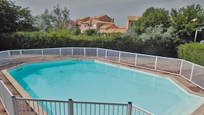 A rectangular swimming pool with a white fence, surrounded by greenery and buildings in the background. - Residence Les Soleillades Et Scarlett (Palavas-les-Flots)
