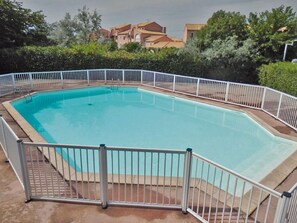 A rectangular swimming pool with a white fence, surrounded by greenery and buildings in the background. - Residence Les Soleillades Et Scarlett (Palavas-les-Flots)