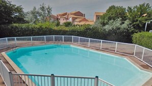 A rectangular swimming pool with a white fence, surrounded by greenery and buildings in the background. - Residence Les Soleillades Et Scarlett (Palavas-les-Flots)