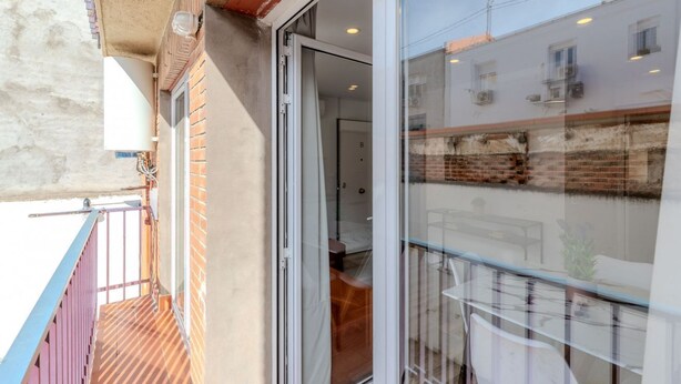 A balcony with a metal railing, a glass door leading to an interior room, and a view of a building with multiple windows. - Bright and Fantastic 1H Apartment Arganzuela (Madrid)