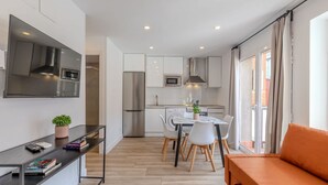 A modern kitchen with white cabinets, a stainless steel refrigerator, and a microwave. There is a dining area with a table and chairs, and a sofa in the foreground. - Bright and Fantastic 1H Apartment Arganzuela (Madrid)