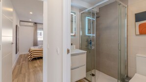 A modern bathroom with a glass shower enclosure, a white sink, and a bed in the adjacent room. - Bright and Fantastic 1H Apartment Arganzuela (Madrid)
