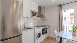 A compact kitchen with a stainless steel refrigerator, a built-in microwave, a washing machine, and a dining area with a table and chairs. - Bright and Fantastic 1H Apartment Arganzuela (Madrid)