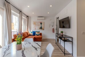 A modern living room with a sofa, a dining table with a potted plant, a TV, and a fireplace. - Bright and Fantastic 1H Apartment Arganzuela (Madrid)