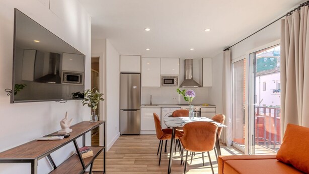 A modern kitchen with a refrigerator, microwave, and oven. There is a dining table with chairs and a sofa.