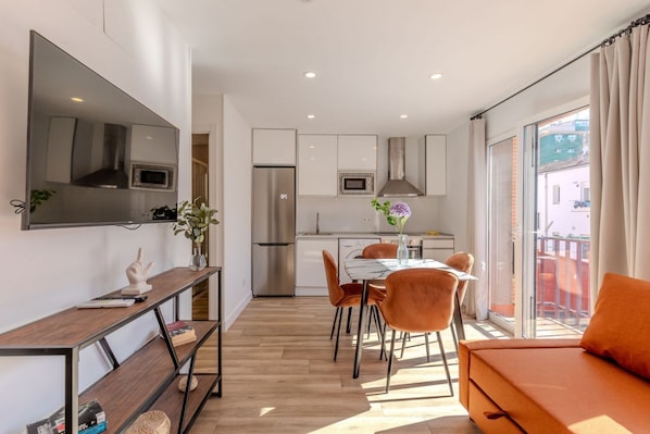 A modern kitchen with a refrigerator, microwave, and oven. There is a dining table with chairs and a sofa.