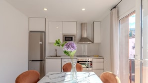 A modern kitchen with white cabinets, a stainless steel refrigerator, a microwave, and a stove. There is a marble table with a vase of flowers.