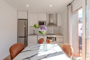 A modern kitchen with white cabinets, a stainless steel refrigerator, a microwave, and a stove. There is a marble table with a vase of flowers.