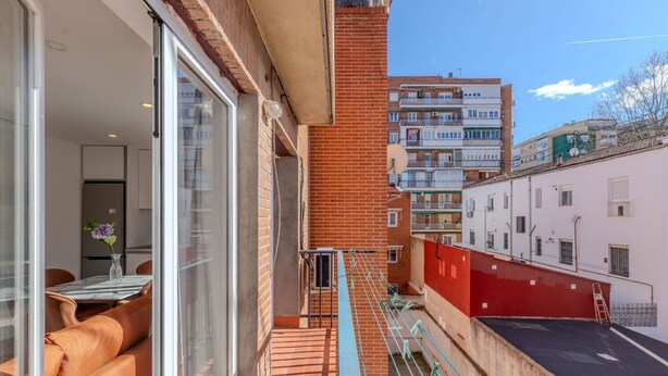 A narrow urban street with a red building, a balcony with orange seating, and a clear sky. - Bright and Fantastic 1H Apartment Madrid Rio (Madrid)