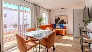 A modern living room with a dining table, orange sofa, and a large window with a view of buildings.
