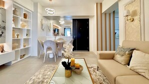 A modern living room with a glass coffee table, a sofa, and a dining area with chairs and a table. - Room-modern Condo Room With City Views i (Davao)