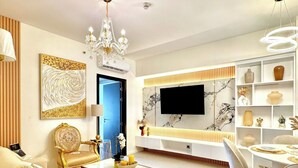 A modern living room with a sofa, coffee table, chandelier, TV, and a dining area with chairs and a table. - Room-modern Condo Room With City Views i (Davao)
