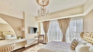 A bedroom with a bed, a desk, a chair, a TV, and a chandelier. - Room-modern Condo Room With City Views i (Davao)