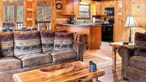 Een knus chaletinterieur met een slaapkamer op de zolder, een woonkamer met leren banken, een houten eettafel en een keukenhoek.