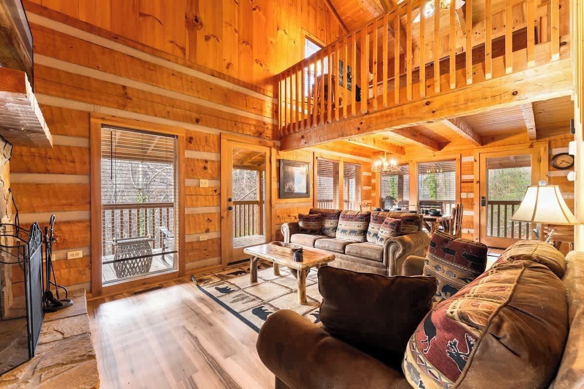 A log cabin interior with a wooden staircase, a sofa set, and a dining area.