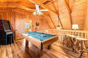 Un interior de madera con mesa de billar, jukebox y ventilador de techo.