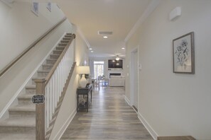 A hallway with a wooden staircase, a flat-screen TV mounted above a fireplace, and a framed floral artwork on the wall. - Stunning and Gorgeous with Comm Pool, Tennis, Pickleball, Bikes, Free Activities Inc Golf @ Bear Tra (Rehoboth Beach)
