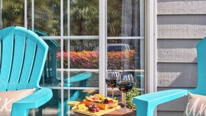 Ein Zimmer mit einem großen Fenster, einem Tisch mit Obstplatte und Weingläsern sowie zwei türkisfarbenen Stühlen.