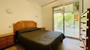 A bedroom with a wooden bed, a nightstand, a dresser, and a sliding glass door leading to a balcony. - 112-PALMAS COSTA: Refurbished flat with capacity for 7 people (SALOU)