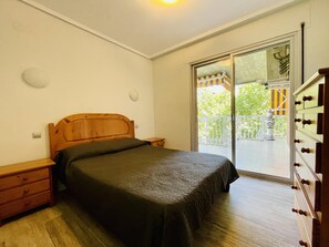 Ein Schlafzimmer mit einem hölzernen Bett, einem Nachttisch, einer Kommode und einer Glastür, die auf einen Balkon führt.
