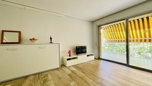 A modern living room with a wooden floor, a white cabinet, a TV, and a balcony with yellow-striped awning. - 112-PALMAS COSTA: Refurbished flat with capacity for 7 people (SALOU)