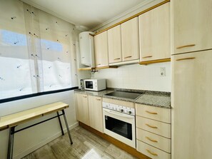 A kitchen with light wooden cabinets, a microwave, a stove, and a window with a curtain. - 112-PALMAS COSTA: Refurbished flat with capacity for 7 people (SALOU)