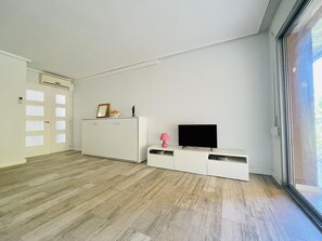 Ein modernes Wohnzimmer mit großem Fenster, Flachbildfernseher, weißem Schrank und Holzboden.