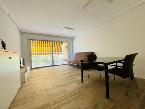 Ein Zimmer mit Esstisch, Stühlen, einer Couch, einem Fernseher und einer Glastür zum Balkon.