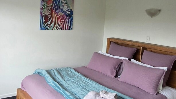 Un lit avec un cadre en bois, une couvre-lit bleue et violette, et un tableau représentant un zèbre accroché au mur.