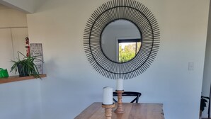 Un coin repas avec une table en bois, des chaises noires, un miroir rond et un panneau affichant les règles de la maison sur le mur.