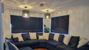 Un salon moderne avec un canapé d’angle foncé, des coussins décoratifs à motifs et deux lampes suspendues.