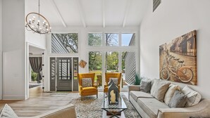 Uma sala de estar espaçosa, com uma janela grande, um candelabro, um sofá, poltronas e uma mesa de centro.
