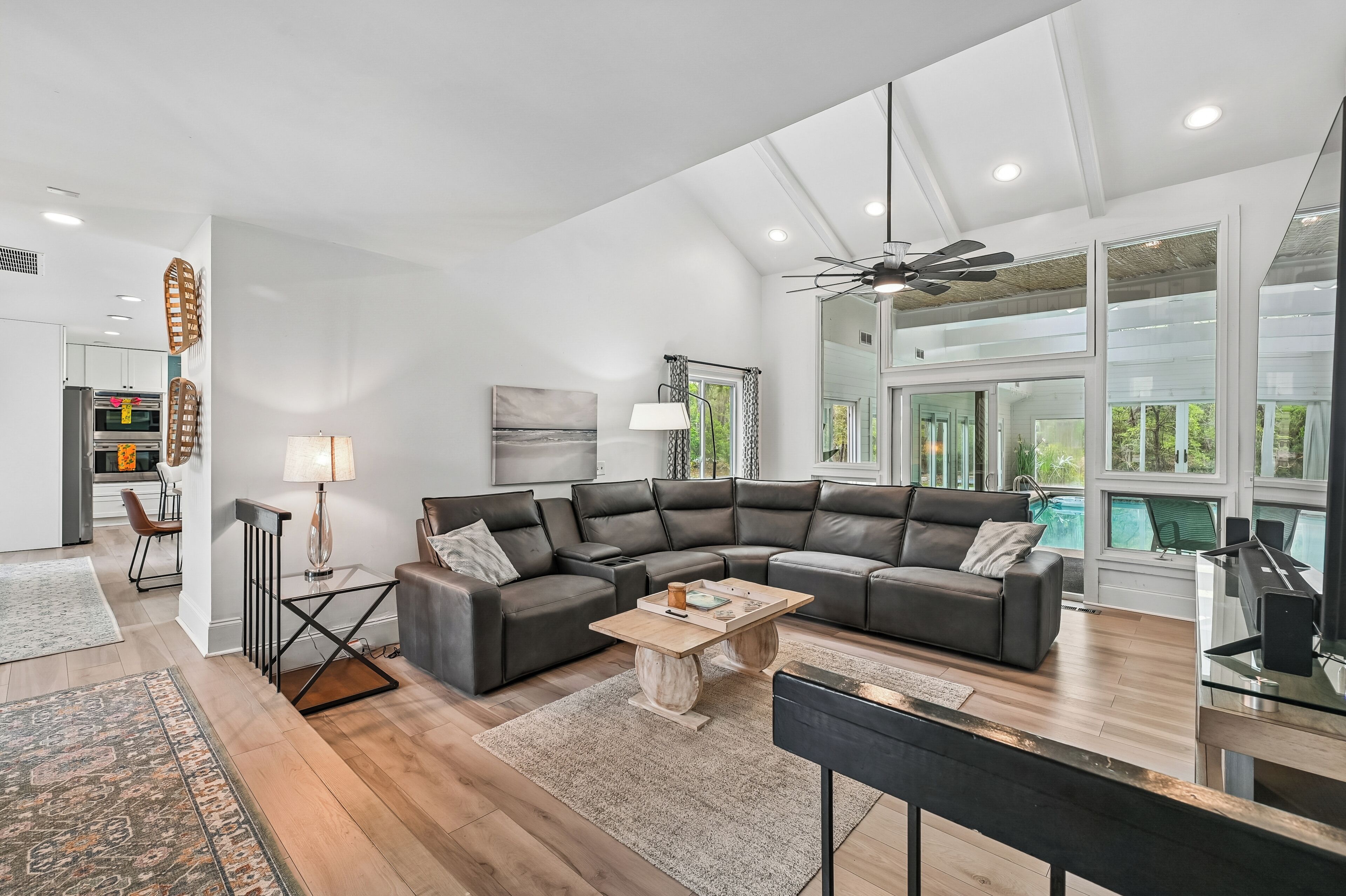 A modern living room with a sectional sofa, a coffee table, a TV, and a large window overlooking a pool.