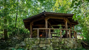 Uma estrutura de madeira rústica com base de pedra, rodeada por uma floresta densa.