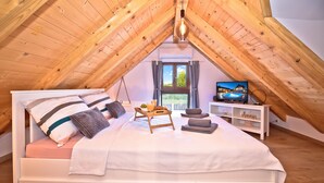 Ett sovrum med ett sluttande tak, en säng med kuddar, ett sängbord med en lampa, en tv och ett fönster med utsikt.
