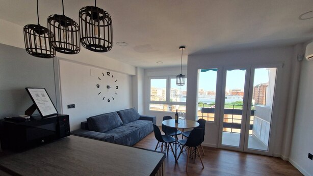 A modern living space with a kitchen, dining area, and large windows offering a city view. - Spacious 3 Bedroom Apartment With Balcony and AC in Castellón (Castelló de la Plana)
