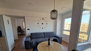 A modern living space with a round wooden table, black chairs, a grey sofa, a wall clock, and a large window offering a city view. - Spacious 3 Bedroom Apartment With Balcony and AC in Castellón (Castelló de la Plana)