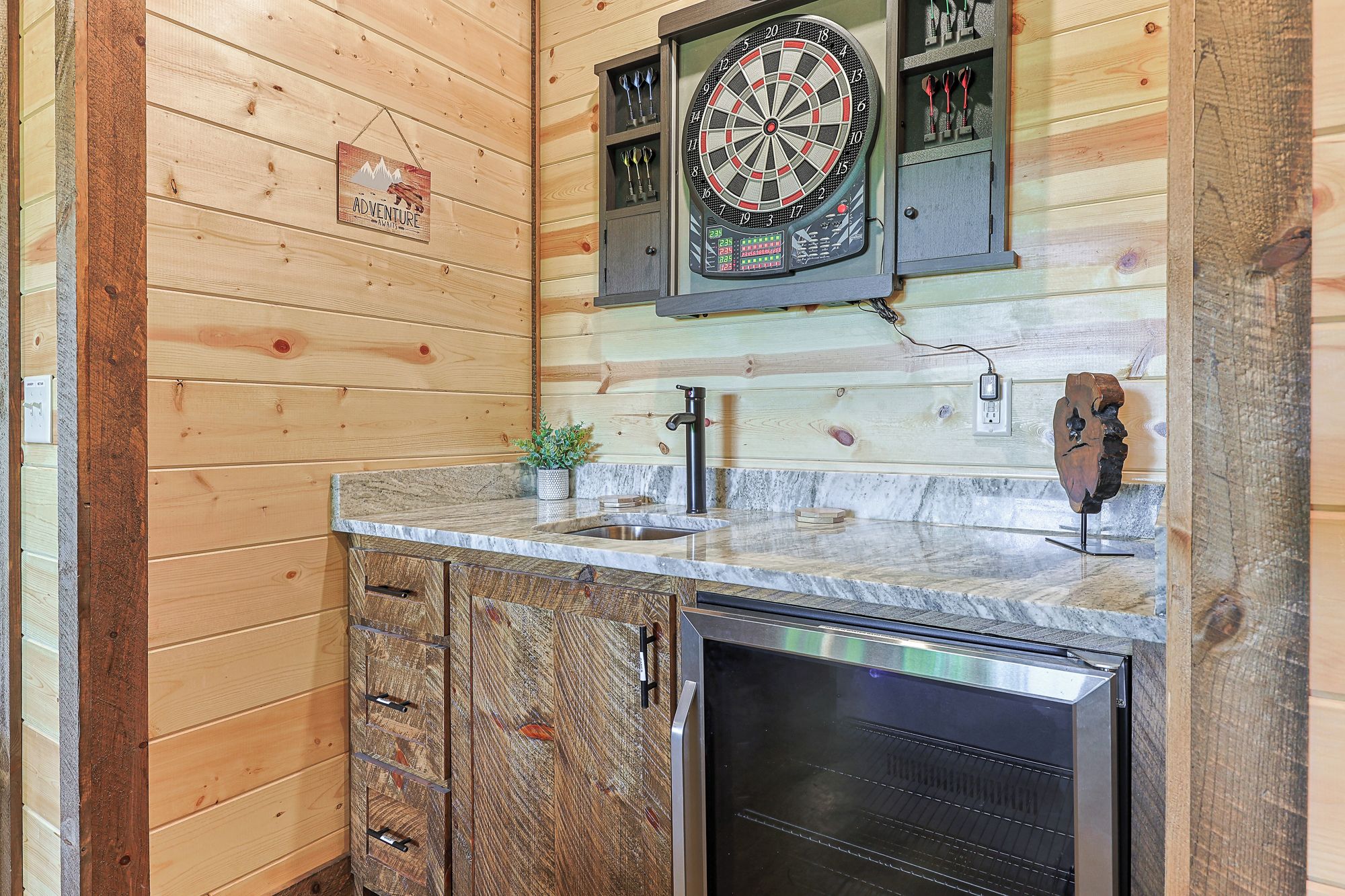 A kitchen with wooden walls, a dartboard, a sink, cabinets, and a microwave.